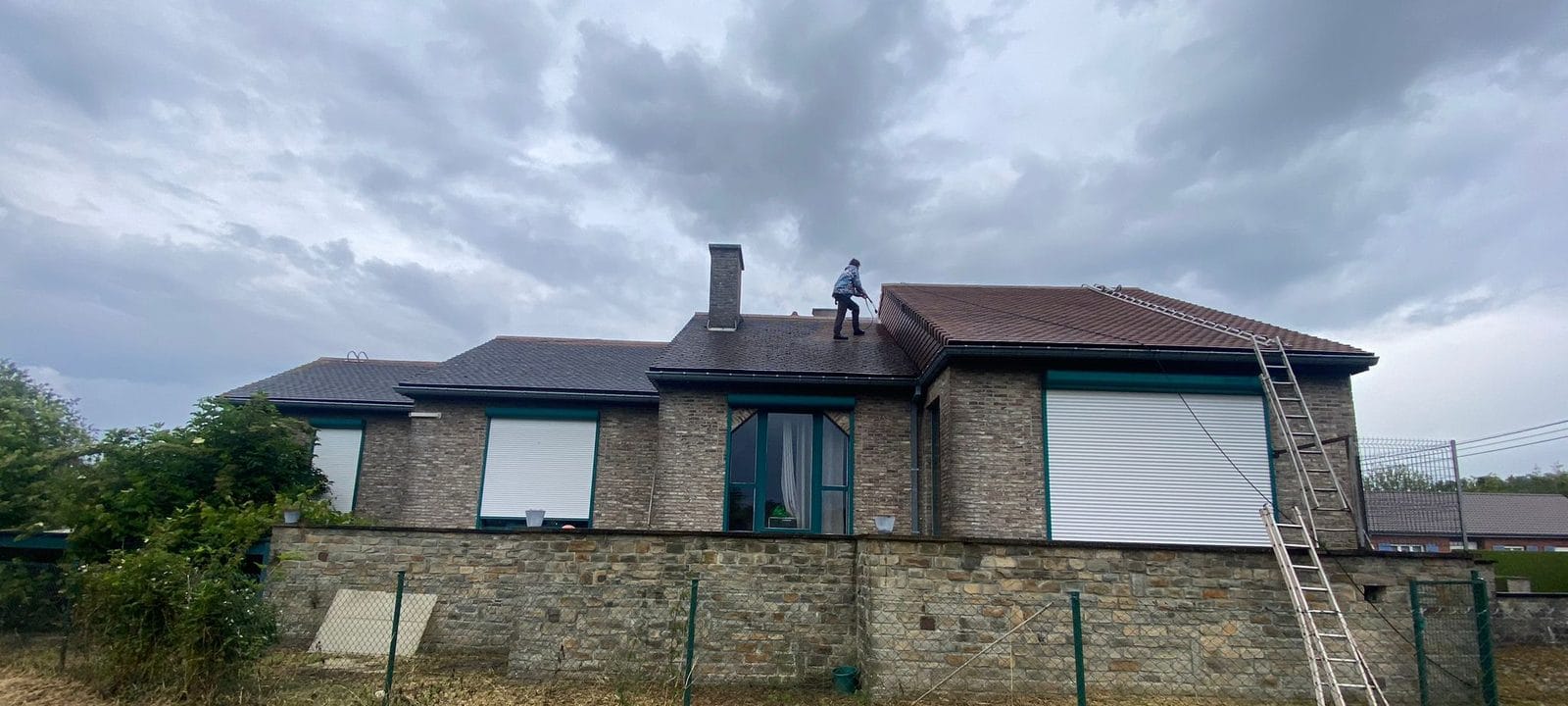 Back of a house with tiled roofs on three levels, a worker on the middle roof