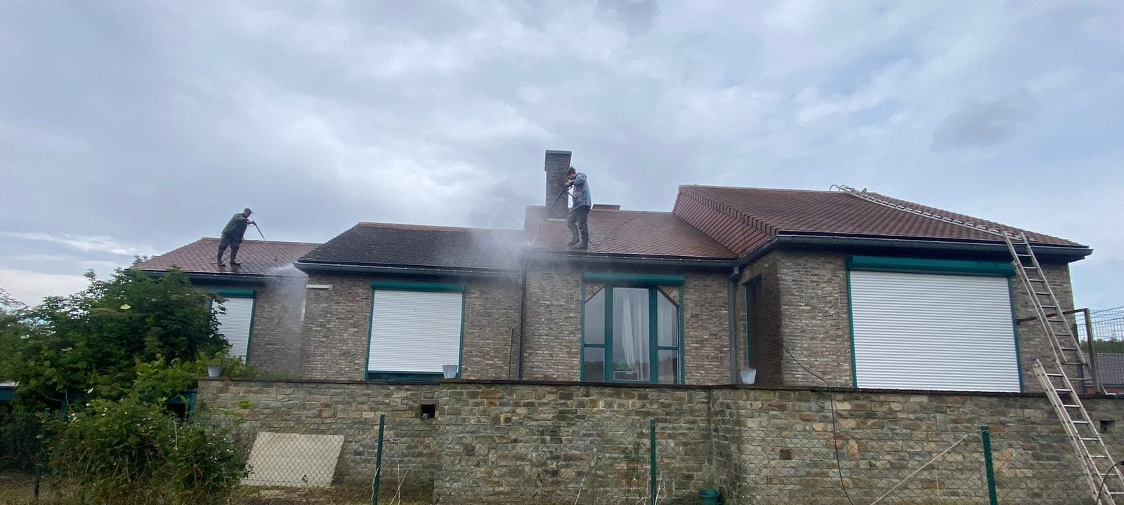 Deux ouvriers démoussent les toitures en tuiles de l'une des trois maisons, vue de l'arrière, à Wadelincourt