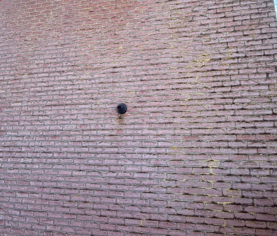 Large section of red brick wall whose joints carry dark marks and a few yellow patches