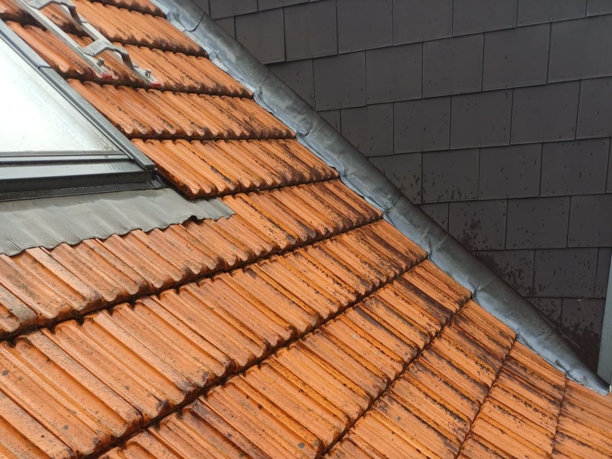 Red tiles with dark marks near a roof window and a lead flashing, seen close up, in Antwerp
