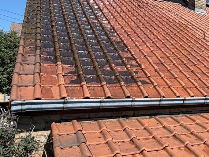 Slope of red tiles with a dark band of moss on the left and lighter cleaned tiles on the right, above the zinc gutter