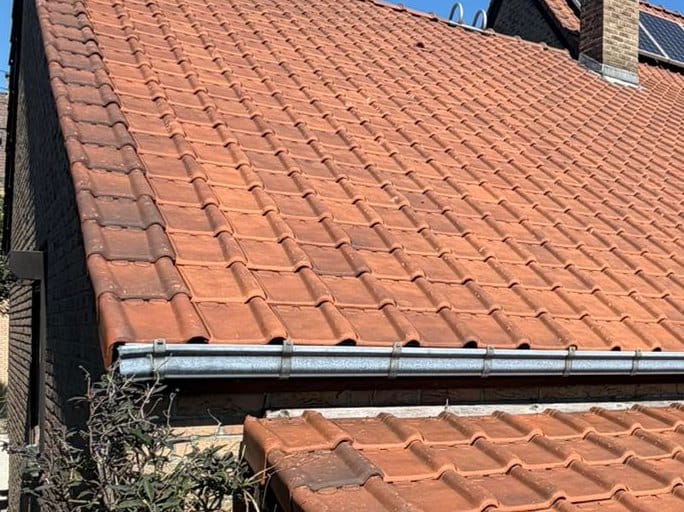 Slope of clean red tiles, from the zinc gutter to the ridge, under a blue sky
