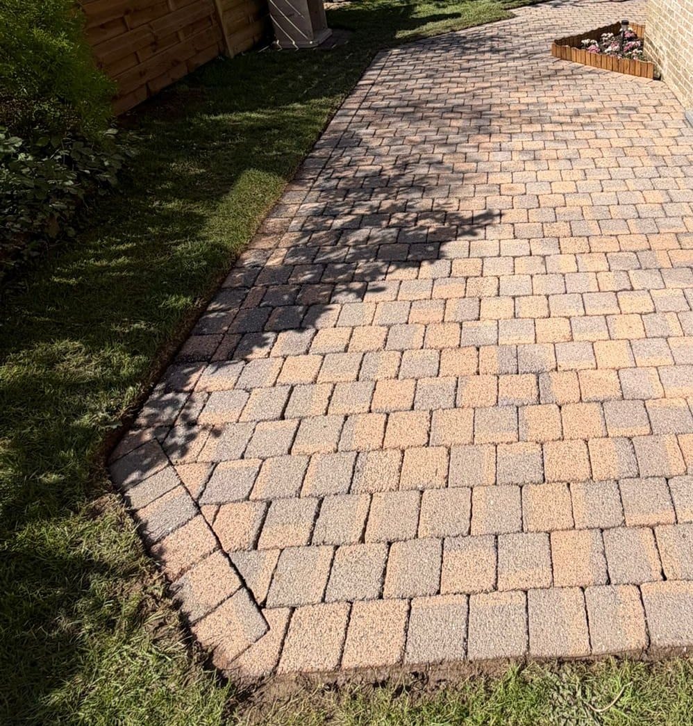 Patio of pink and beige pavers, edged with lawn and a wooden fence, in Chaumont-Gistoux