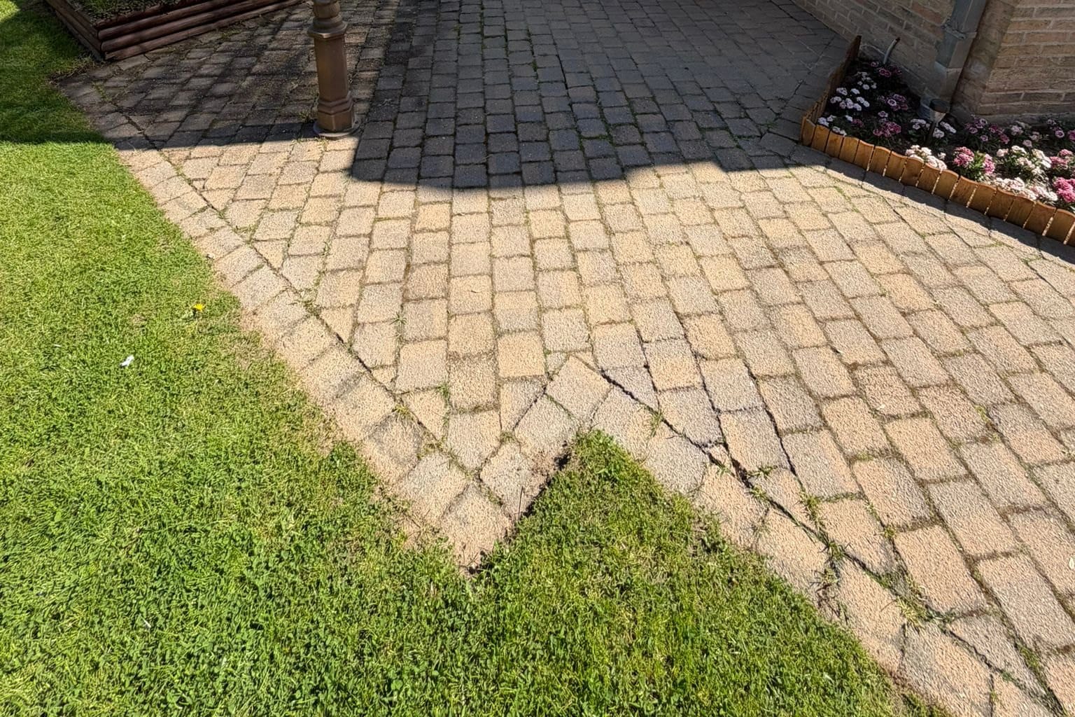 Patio pavers with joints filled with grass and dirt, in the shade of a pergola and in the sun, flower bed and lawn