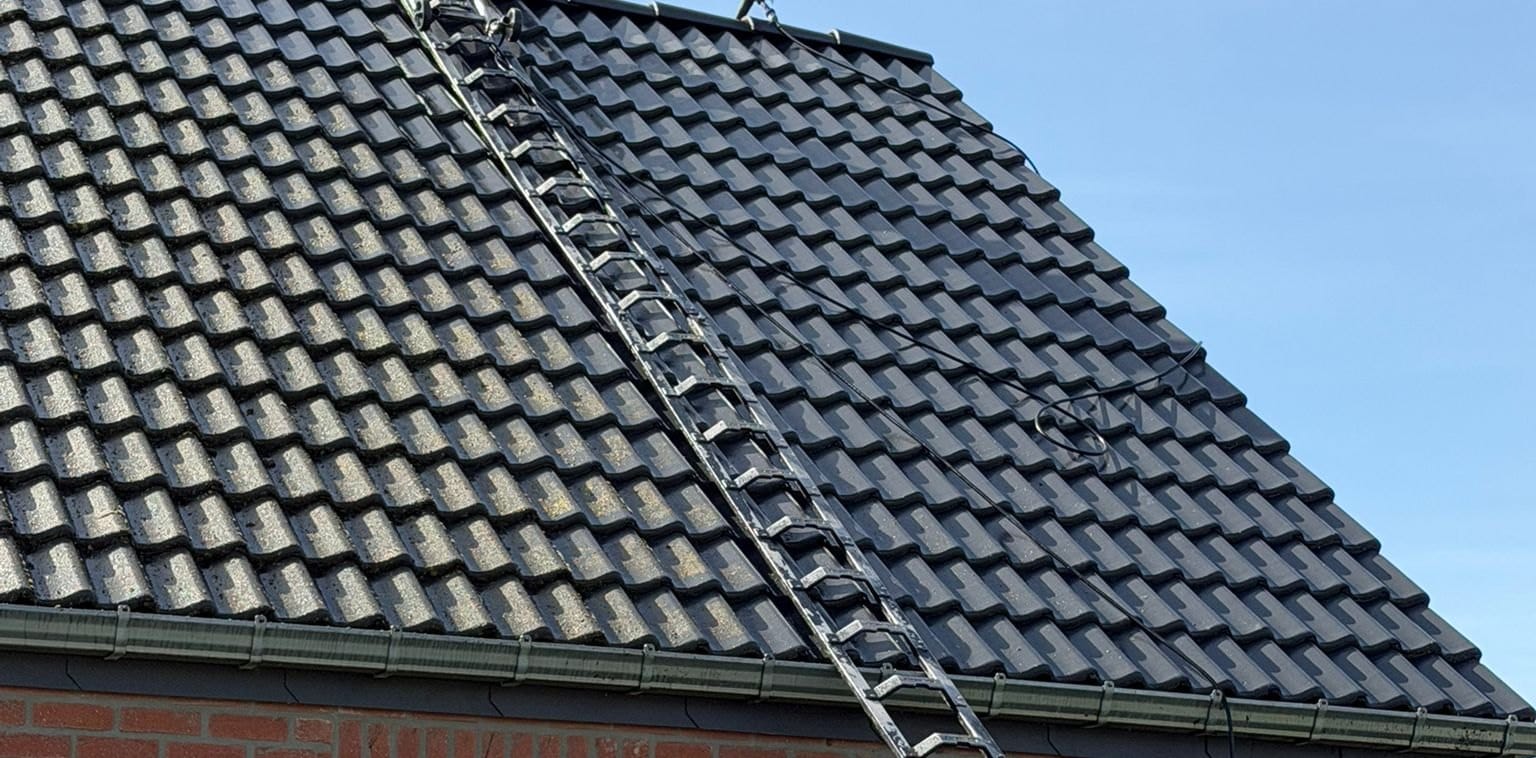 Versant de tuiles anthracite avec une échelle de toit : à droite de l'échelle, des tuiles sombres et unies, à gauche des tuiles grises tachées, gouttière en bas