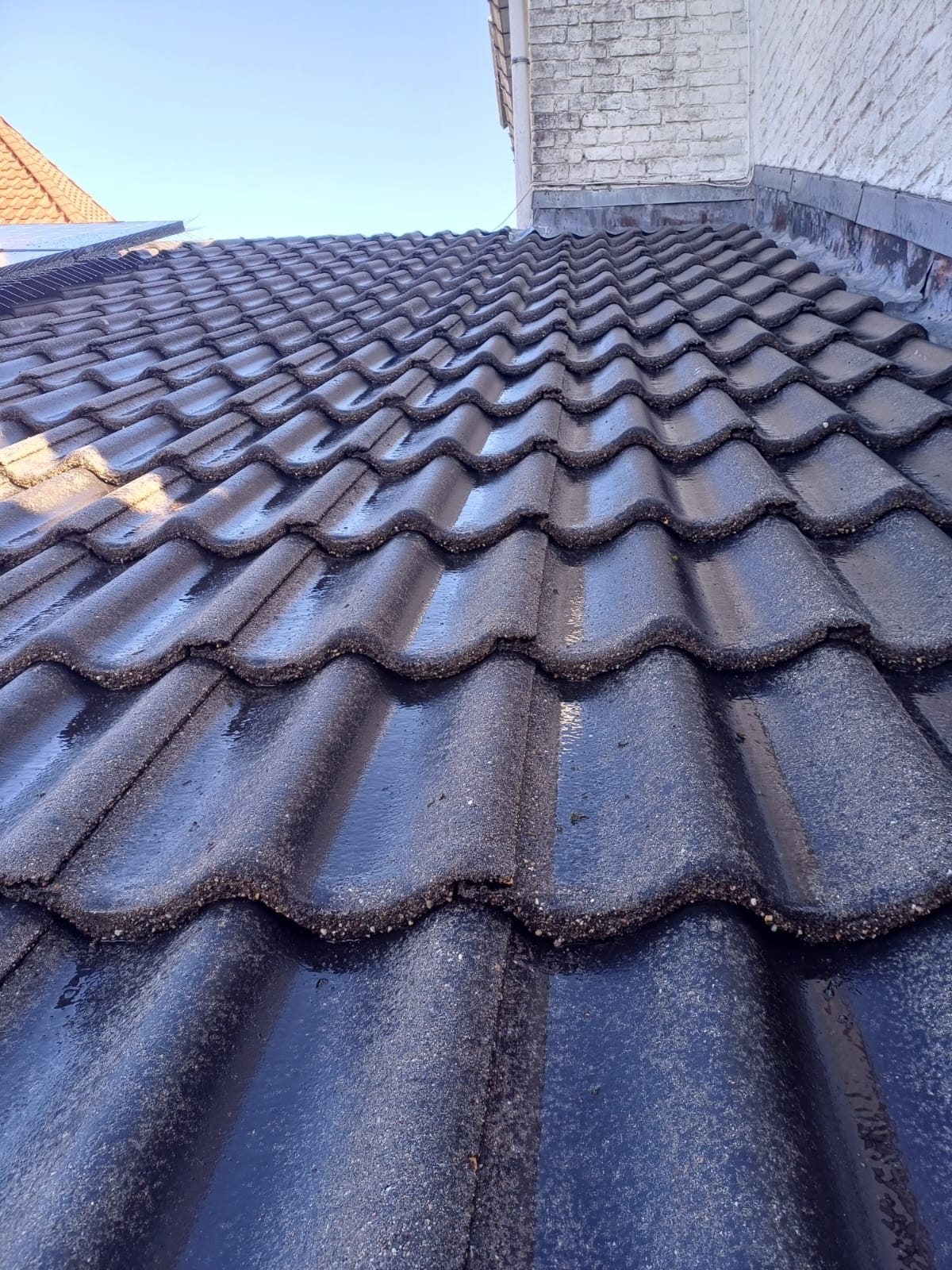 Slope of clean wet dark tiles, with no moss, along a light brick wall