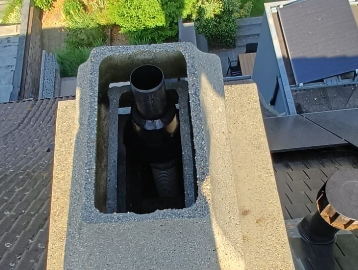 The same concrete chimney seen from above, light-coloured and clear of lichen, dark tiles around
