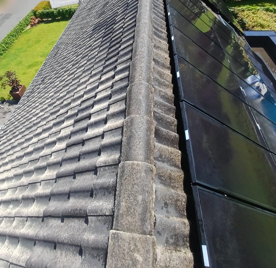 The same ridge of a tiled roof seen from above, cleared of its moss, next to solar panels, in Hastière