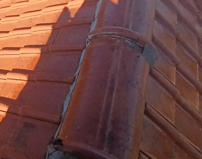 Ridge of red tiles seen close up, with the red tiles of both slopes on either side