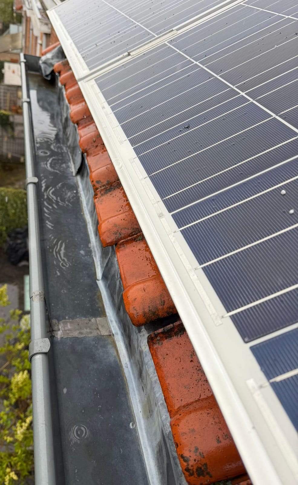 Zinc gutter at the edge of a roof, red tiles stained with moss and solar panels edged in white