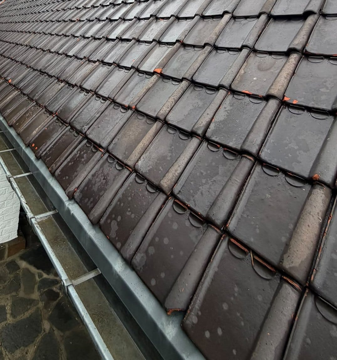Large slope of wet brown tiles along a zinc gutter, seen from the top of the roof, in Overijse