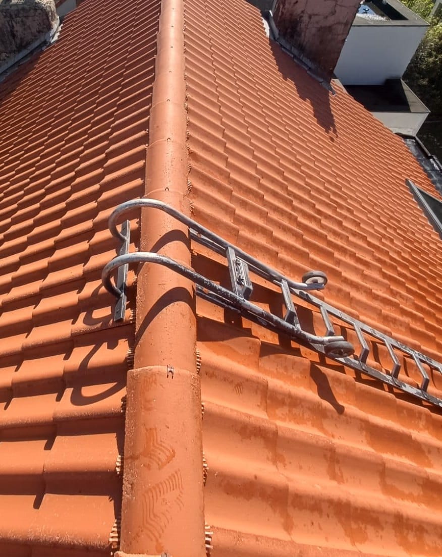 Red-tiled roof seen from the ridge, roof ladder set on a slope, chimneys at the top of the picture