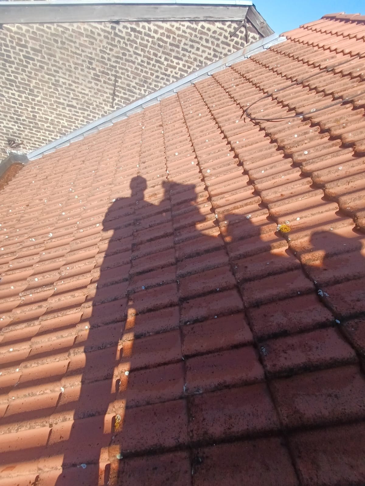 Slope of red tiles dotted with white spots of lichen and dark lines of moss, brick wall and zinc flashing at the top
