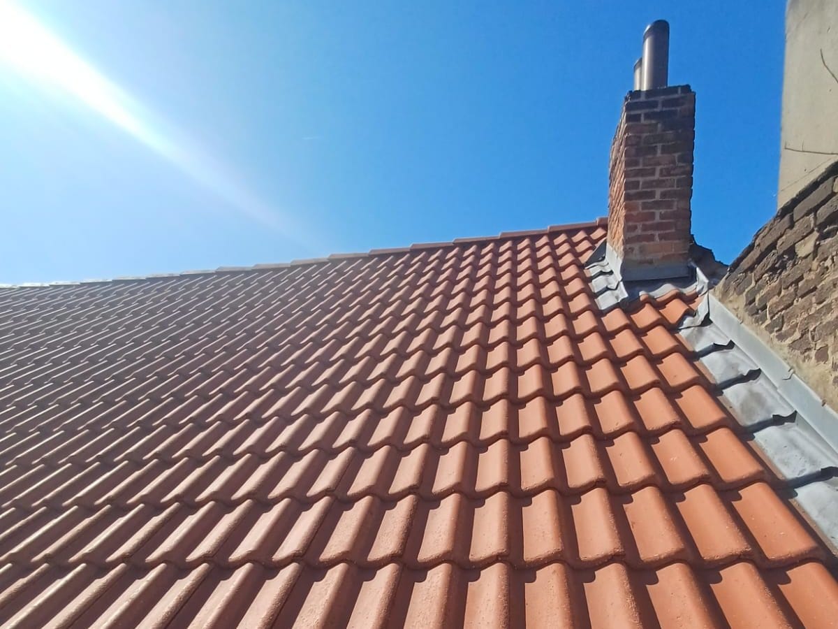 Slope of red tiles in uniform shades and a brick chimney under a blue sky