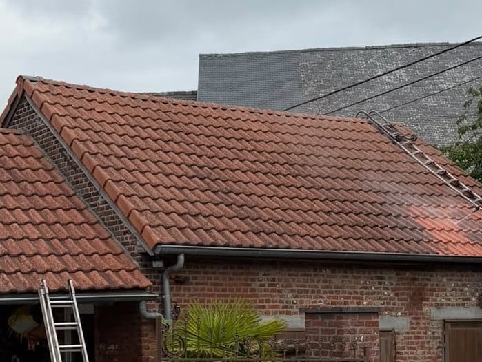 Roof of red tiles under an overcast sky, a roof ladder set on the slope and a lighter band of tiles on the right, a ladder leaning against the gutter of the neighbouring roof