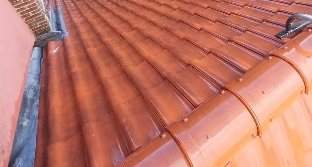 Versant de tuiles rouges brillantes d'humidité, mur en briques à gauche, crochet de sécurité et faîtage à droite