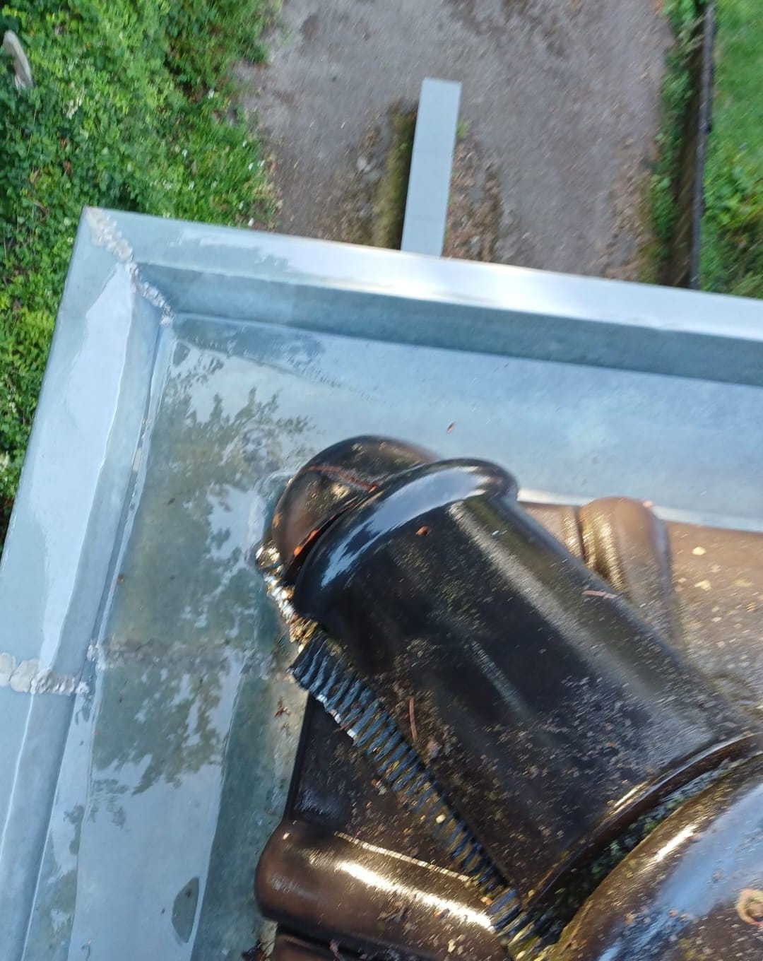 Corner of a wet zinc gutter, with its soldered joints, at the edge of dark tiles